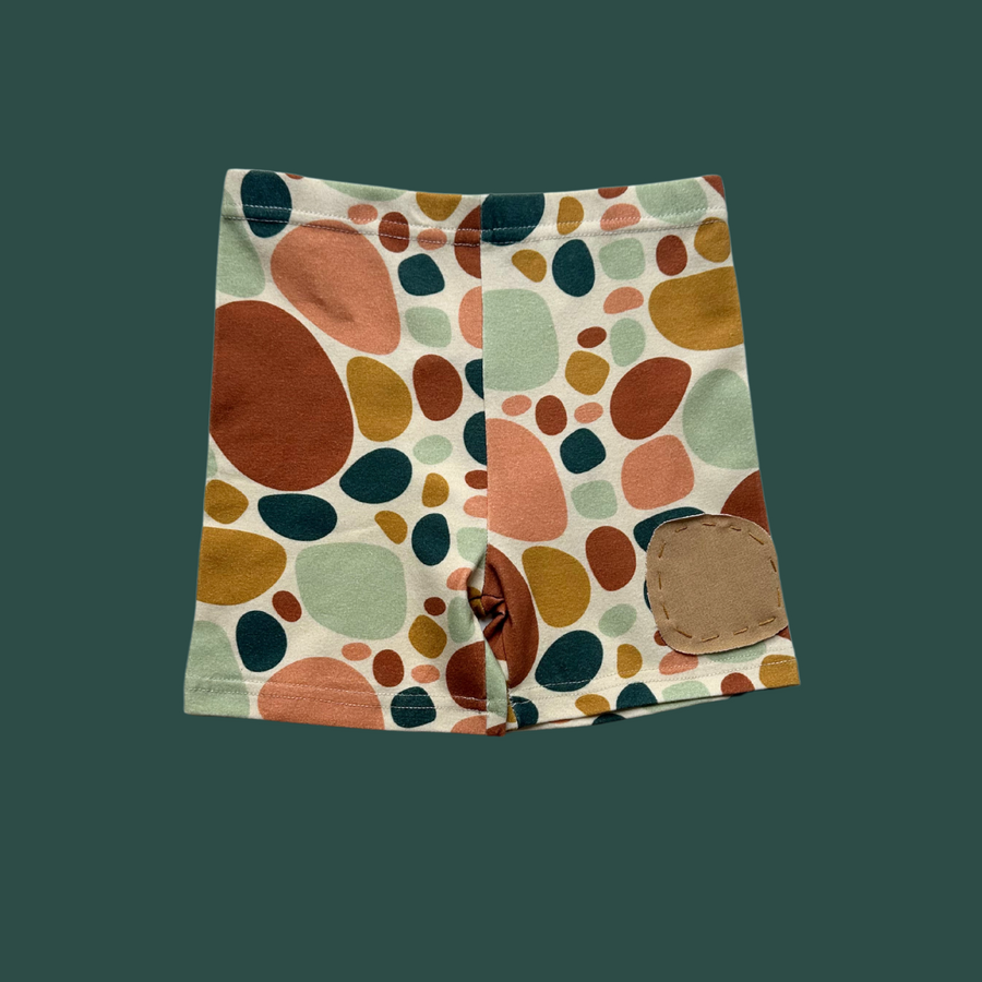 More The Label organic cotton children's clothing stone print bike short front flat lay on dark green background.