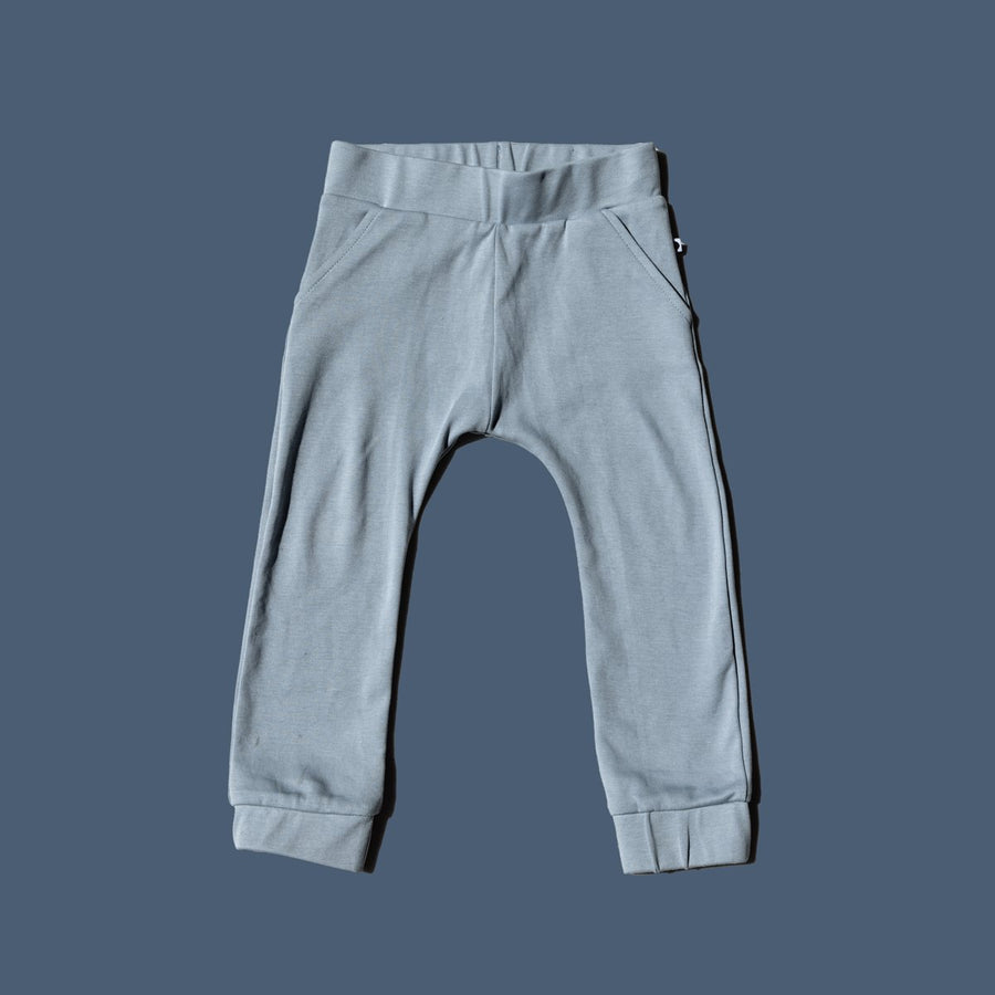Flay lay image of More the label dusty blue track pant on blue background. 