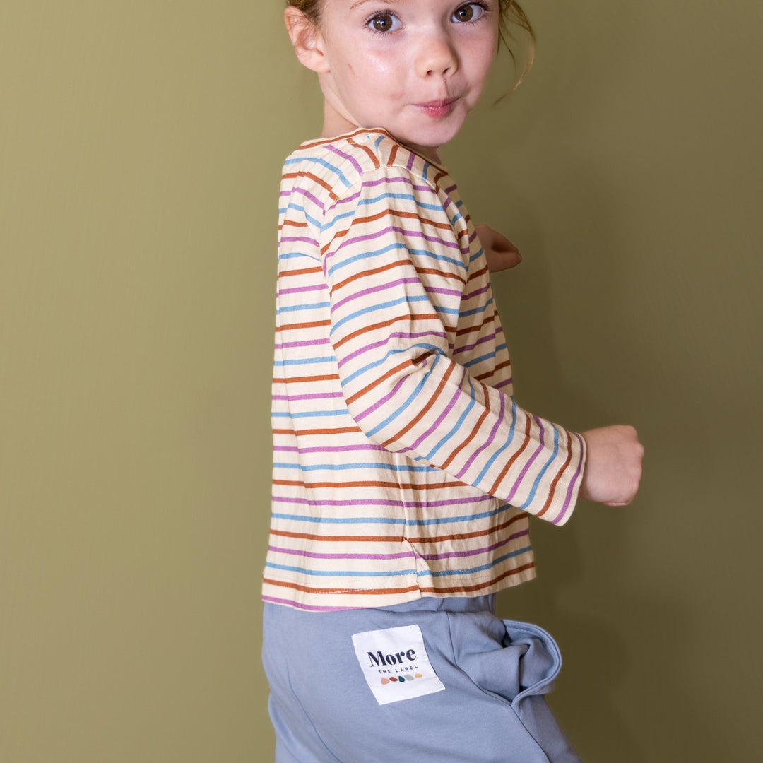 Photo of child pulling a cheeky face while wearing More the label striped long sleeve tee and dusty blue track pant.