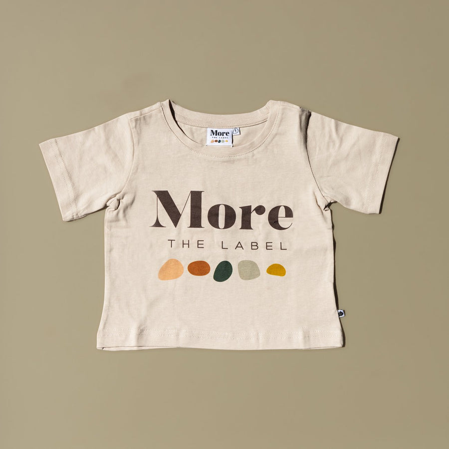 Flat lay image of More the label logo tee on green background.