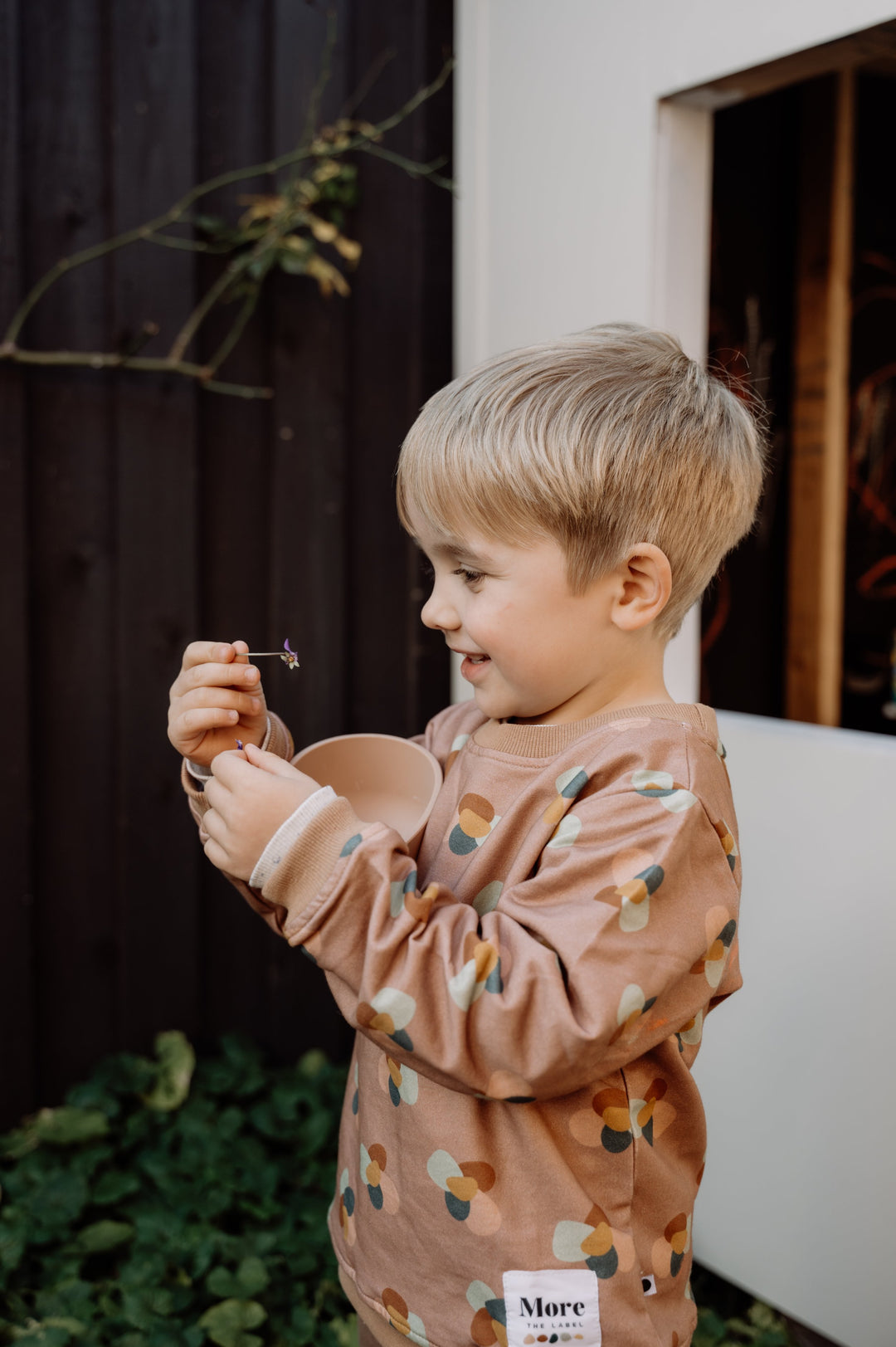 Photo of four year old child wearing More the label stone huddle jumper while playing with flowers.