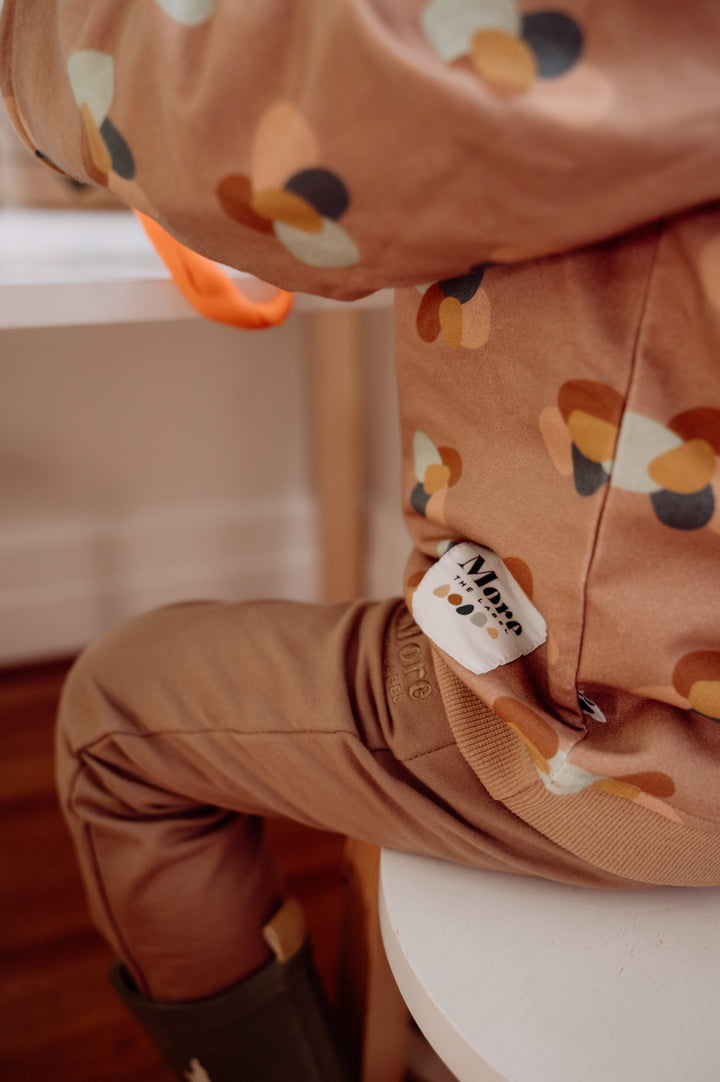 Close up image of child sitting on chair wearing More the label stone huddle jumper and chocolate brown track pant.
