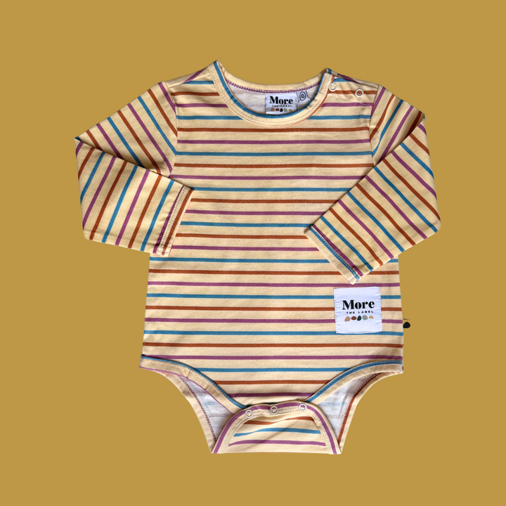 More The Label striped organic cotton baby bodysuit flatlay image on gold background. Snap button opening at lefthand shoulder is un fastened as is the snap closure at crutch. Features MTL logo patch
