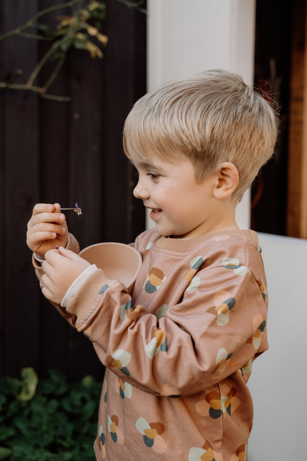 Photo of four year old child wearing More the label stone huddle jumper while playing with flowers.