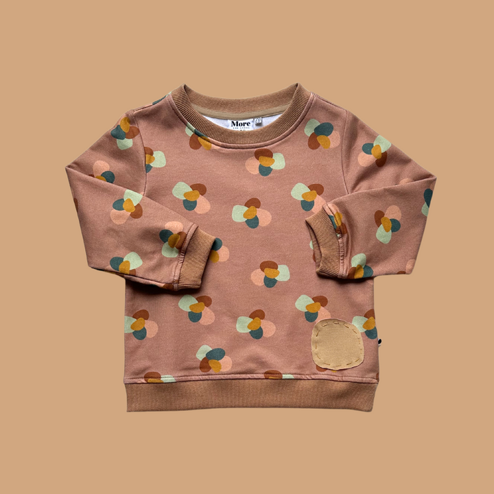 More The Label organic cotton children's clothing Stone Huddle Jumper flat lay image of front of garment on peach background. Garment features custom stone huddle print and hand stitched stone detail.