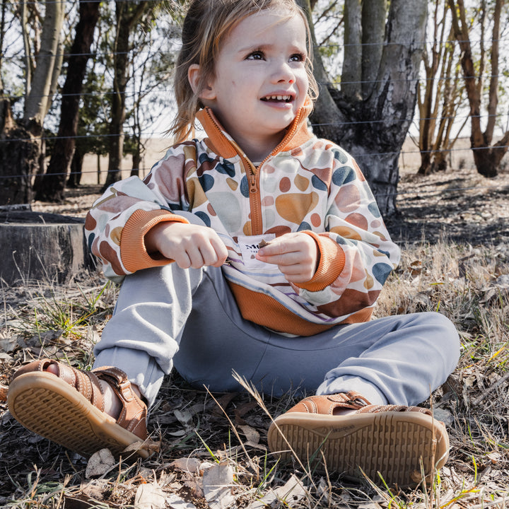 Image of More The Label organic cotton children's clothing Stone Print Jumper, child sitting in Australian bush.