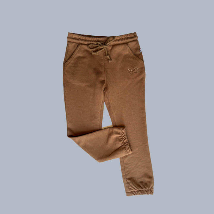 More The Label organic cotton children's clothing chocolate track pant flat lay image of front on a blue background. Brown track pants with elastic waste and drawstring. 