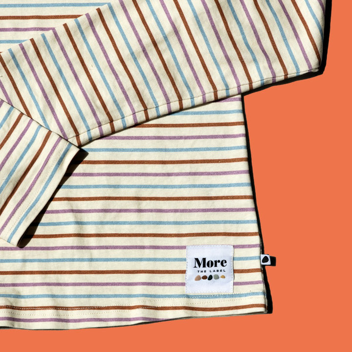 Close up flat lay image of More the label striped long sleeve top on burnt orange background.