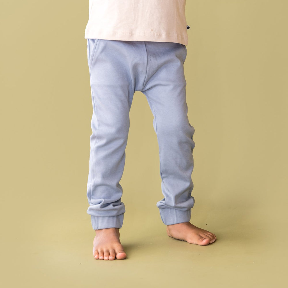 Close up image of child wearing More the label dusty blue track pant with logo tee on top. 
