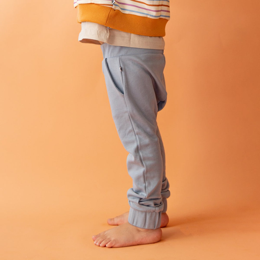 Close up of child wearing More the label dusty blue track pant with logo tee and stone print pullover on top. 