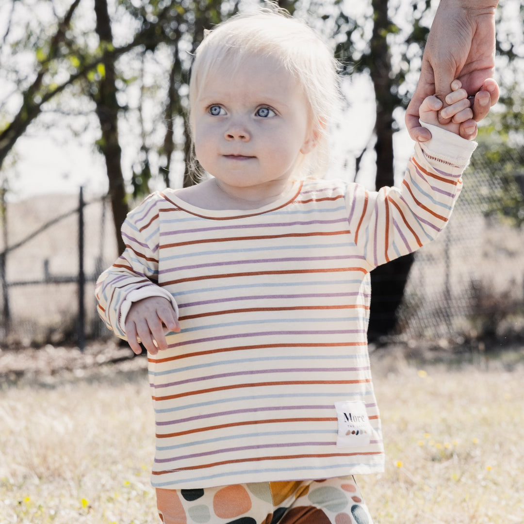 Image of one year old child holding parents hand, wearing More the label striped long sleeve tee.