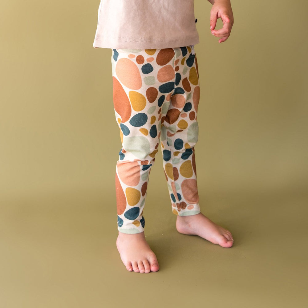 Close up image of child wearing More the label stone print legging with logo tee and bare feet.