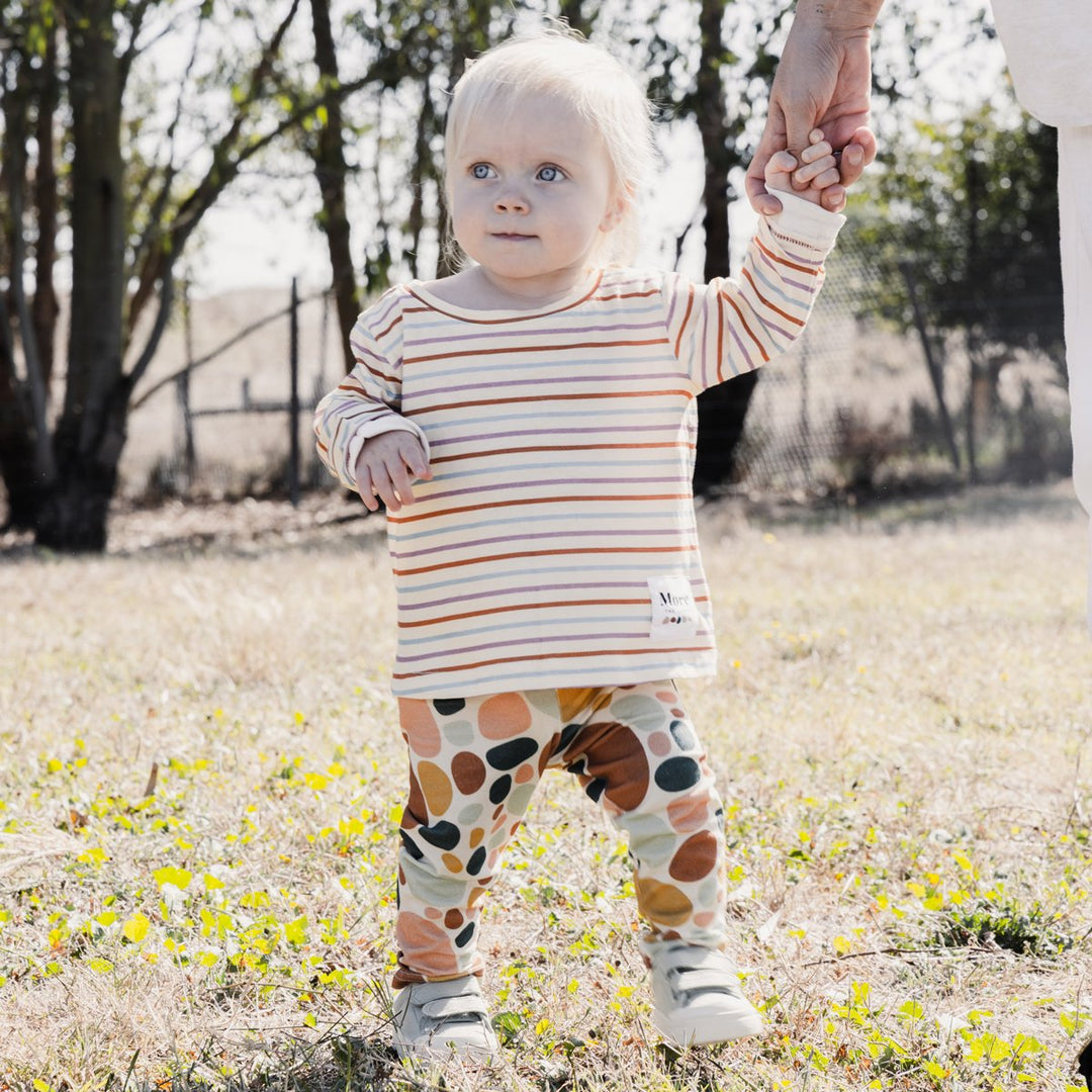 Photo of child holding parents hand wearing More the label stone print legging with striped long sleeve tee.
